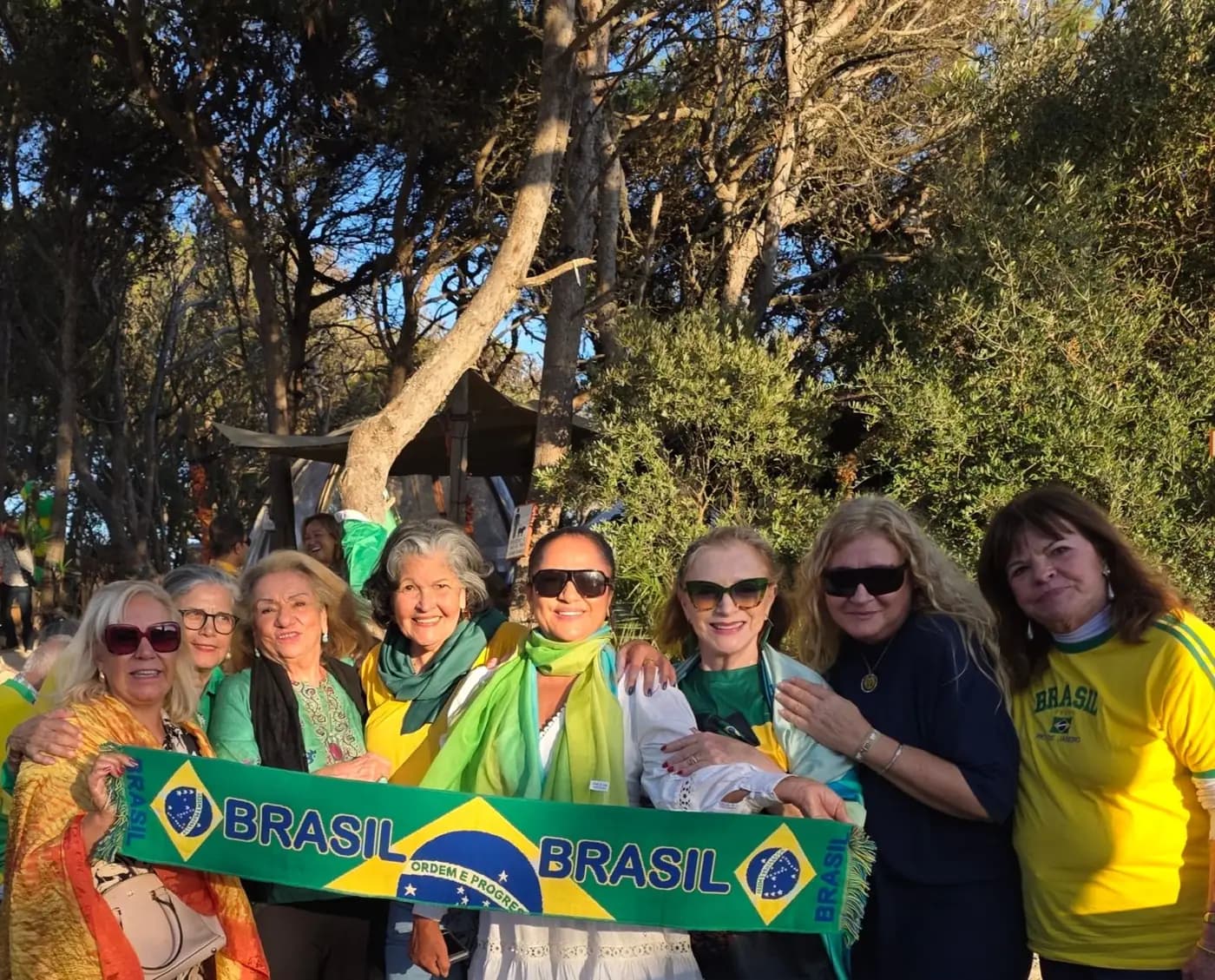 Grupo de associadas segura uma faixa do Brasil sob os pinheiros do espaço da festa