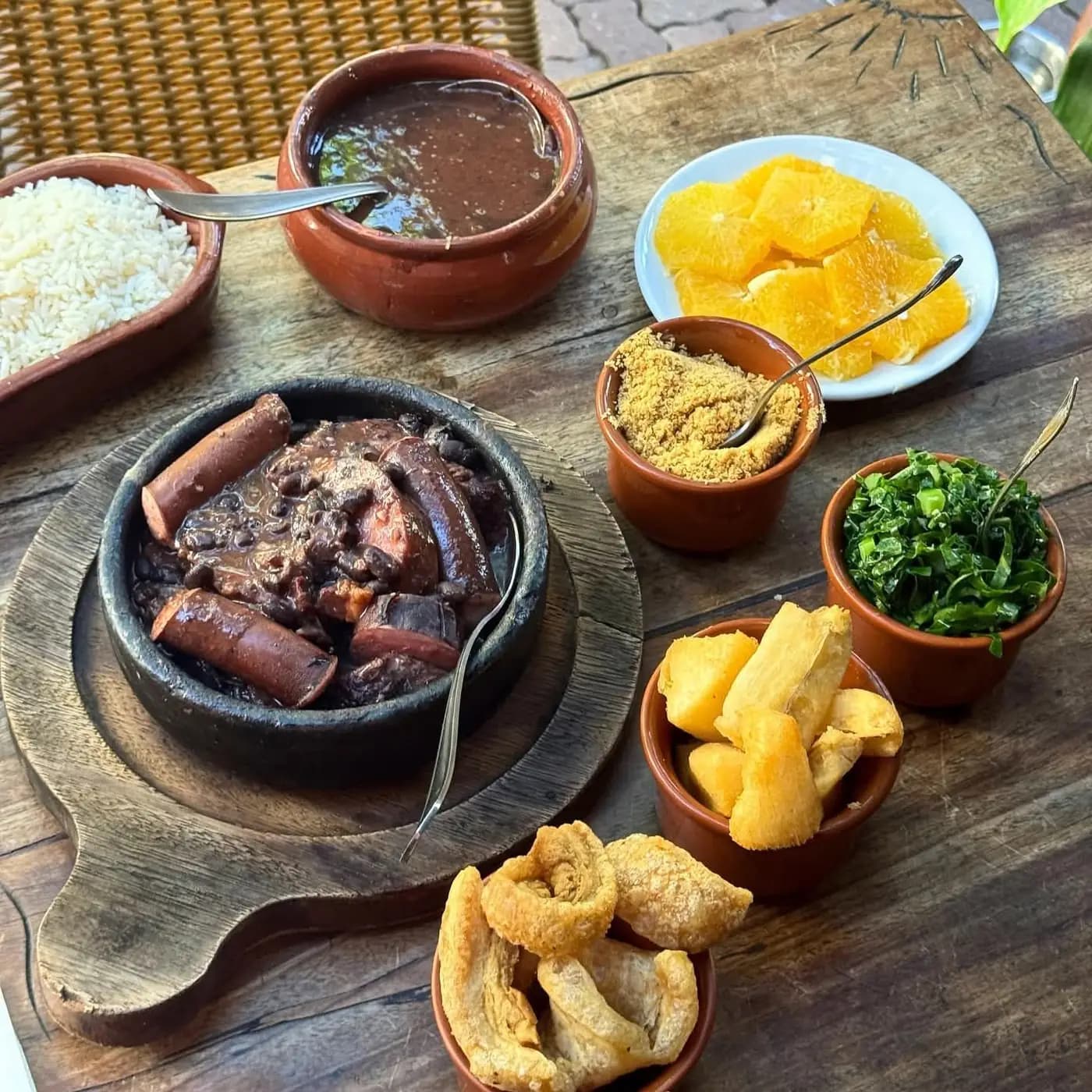 Feijoada completa servida à mesa, com farofa, couve e laranja