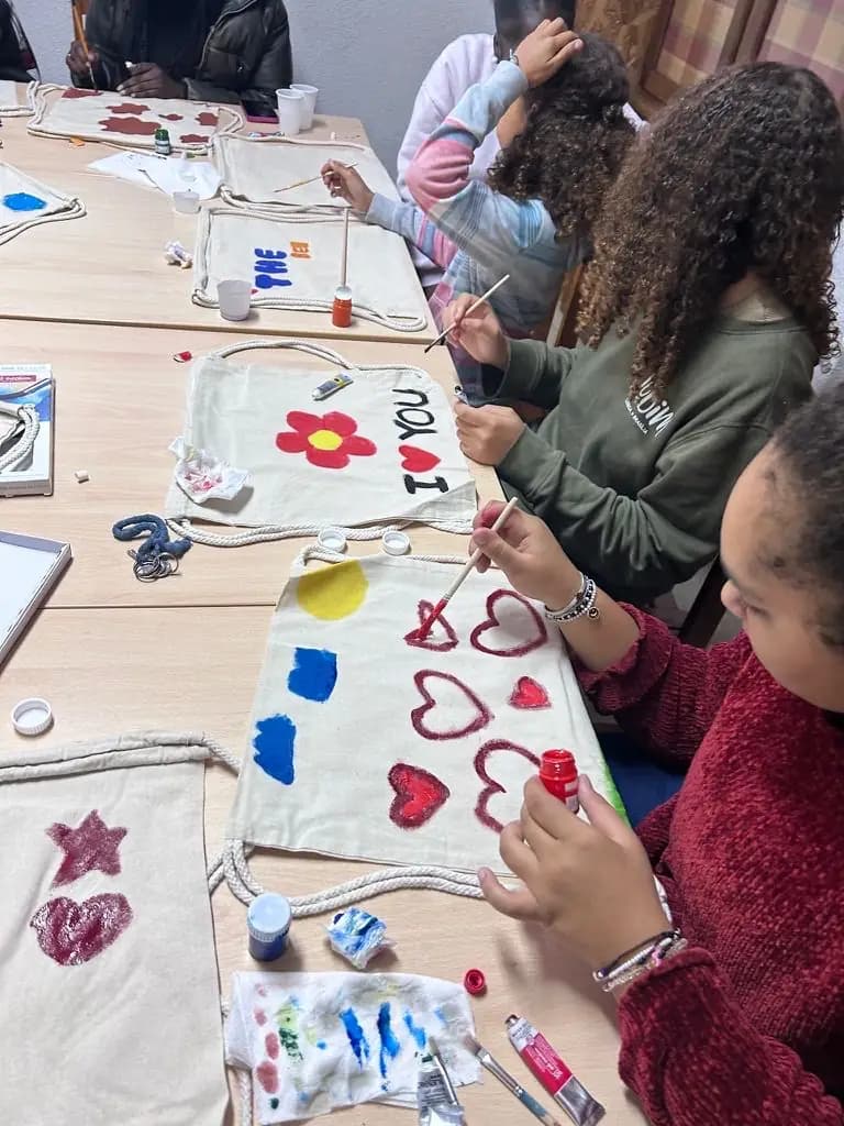 Crianças concentradas a pintar, com as tintas espalhadas pela mesa